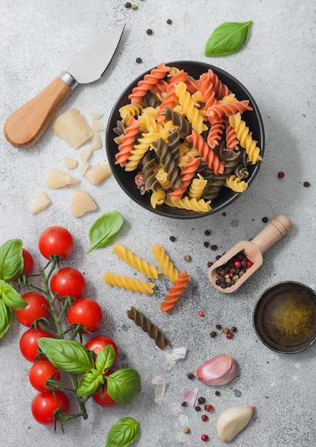 Verse rauwe tricolore fusilli pasta in zwarte kom met kerstomaatjes en basilicum knoflook en olie met Parmezaanse kaas op lichte tafel achtergrond Bovenaanzicht