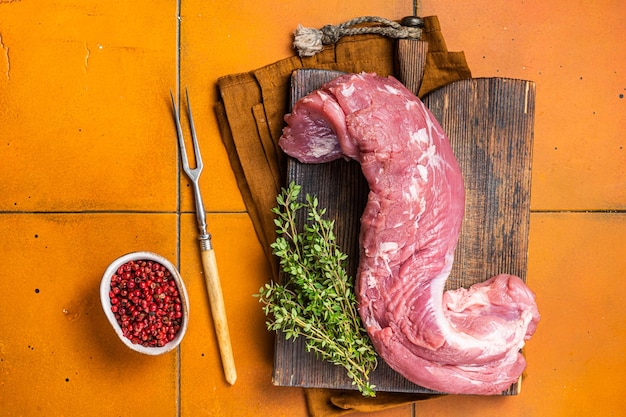 Verse rauwe varkenshaas filet vlees op een houten bord met tijm oranje achtergrond bovenaanzicht