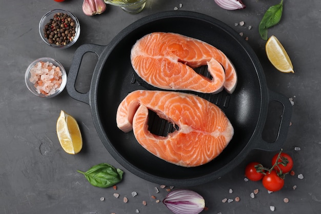 Verse rauwe zalmsteaks in een grillpan en ingrediënten op een donkere achtergrond Uitzicht van bovenaf