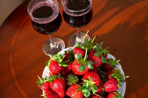 Verse rijpe aardbeien en glazen rode wijn op de achtergrond