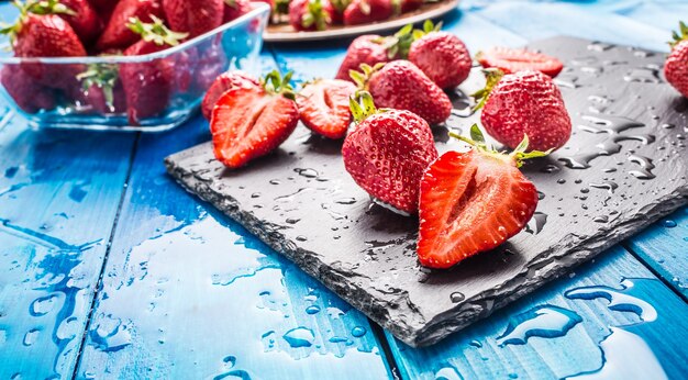 Verse rijpe aardbeien gewassen met water op blauwe tafel.