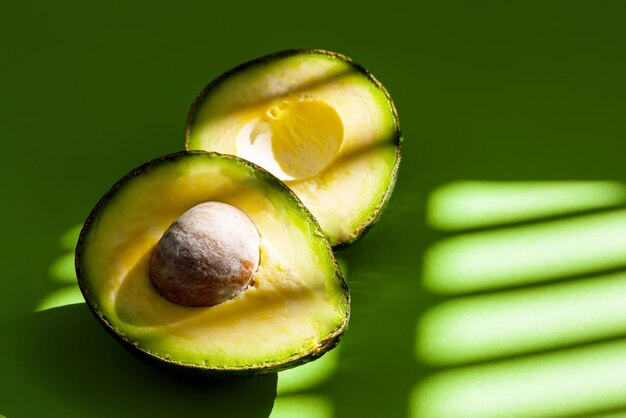 Foto verse rijpe avocado in tweeën gesneden op de groene achtergrond met schaduwen van natuurlijk zonlicht