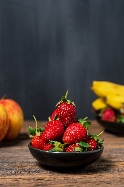 Verse rijpe biologische aardbei in een zwarte kom op houten tafelsteen of betonnen ondergrond