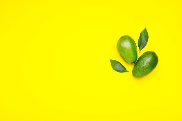 Verse rijpe biologische groene avocado's met bladeren op een gele zomerachtergrond in kleur met kopieerruimte