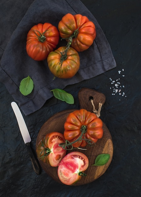 Verse rijpe haarlooftomaten en basilicumbladeren op rustieke houten raad over zwarte steen.