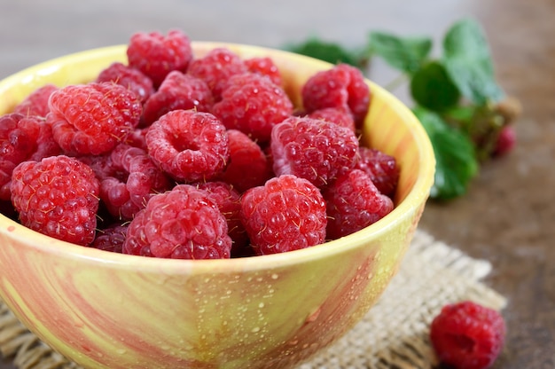 Verse rijpe smakelijke frambozen in een gele keramische kom. Zomer bessen.