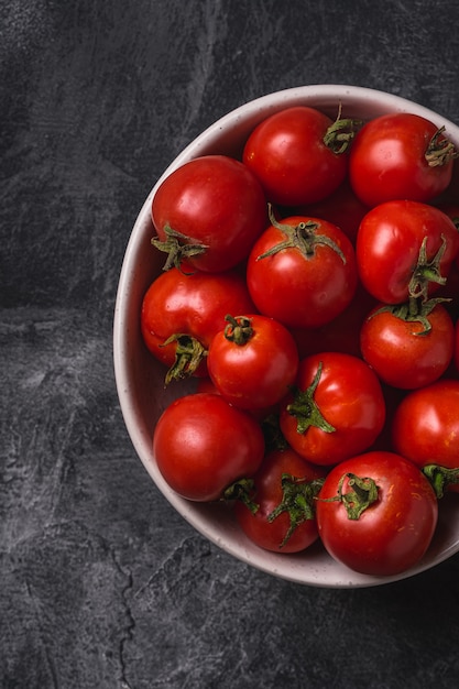 Verse rijpe tomaten in kom op donkere betonnen ondergrond