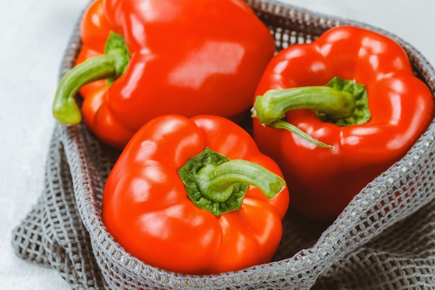 Verse rijpe zoete rode paprika in milieuvriendelijke herbruikbare zak op grijze achtergrond Close-up