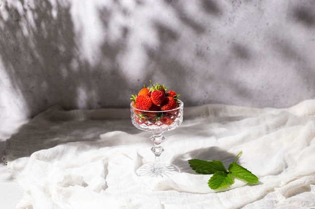 Verse rode aardbeien in een glas in de schaduw van bloemen op een tafel op een betonnen ondergrond.