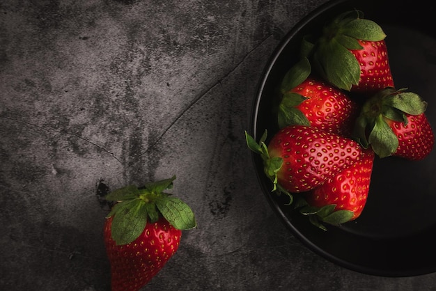 Verse rode aardbeien in kom. Aardbeivruchten op donkere stenen tafel kopieer ruimte voor tekst. bovenaanzicht.