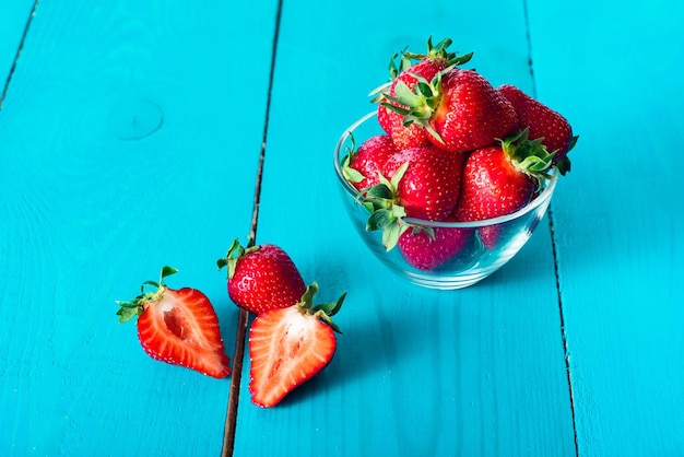 Verse rode aardbeien in transparante kom en kleine keukenhanddoek op blauwe houten achtergrond