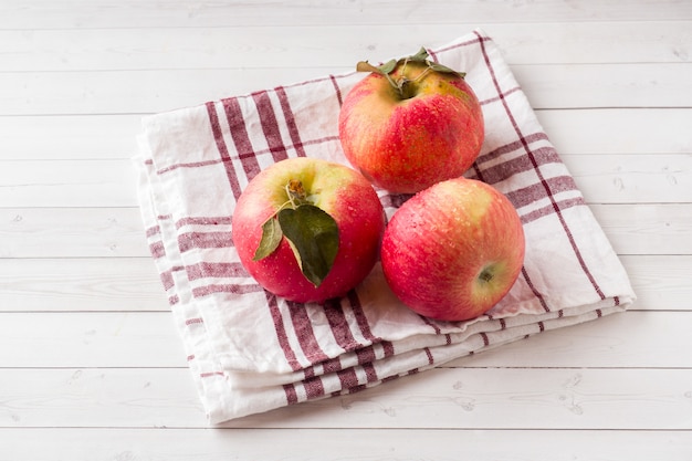 Verse rode appels met groene bladeren op een servet. Licht houten oppervlak.