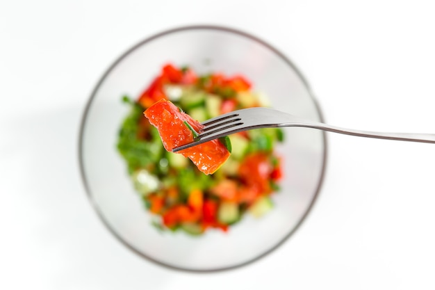 Verse rode tomaat op een vork. Frisse salade met groenten, tomaten, komkommers, sla, saladebladeren op witte bovenaanzicht als achtergrond. Gezond voedsel en dieetconcept. Vegetarisch eten