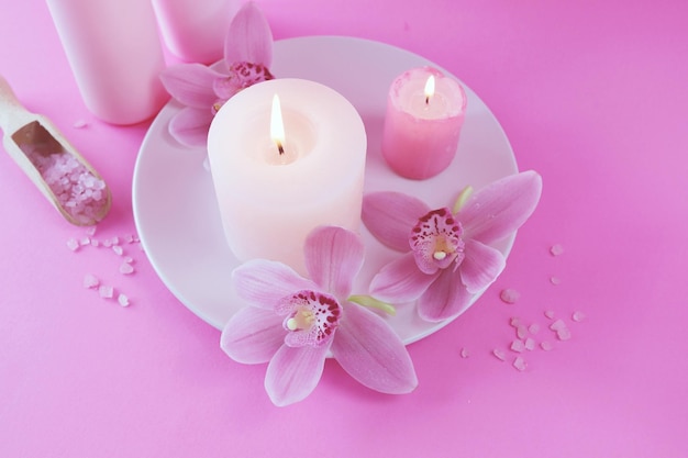 Verse roze orchidee bloemen brandende kaarsen zeezout op een helder roze achtergrond spa concept