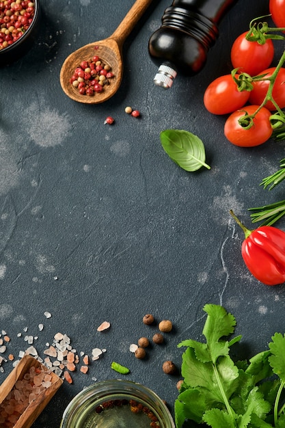 Foto verse rozemarijn, koriander, basilicum, kerstomaatjes, paprika en olijfolie, kruiden, kruiden en groenten aan zwarte leisteentafel.