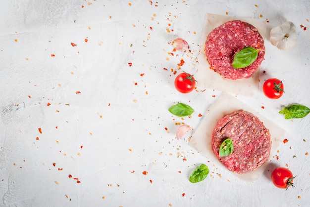 Verse ruwe eigengemaakte fijngehakte rundvleeslapje vleesburger met kruiden, tomaten en basilicum, op een witte steen concrete lijst, hoogste mening