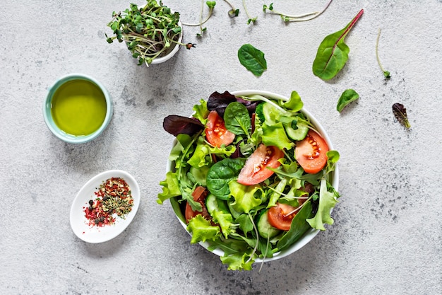 Verse salade met verse groenten, rijpe tomaten, komkommersla en microgroen in een kom op een grijze achtergrond Gezond rauw voedselconcept
