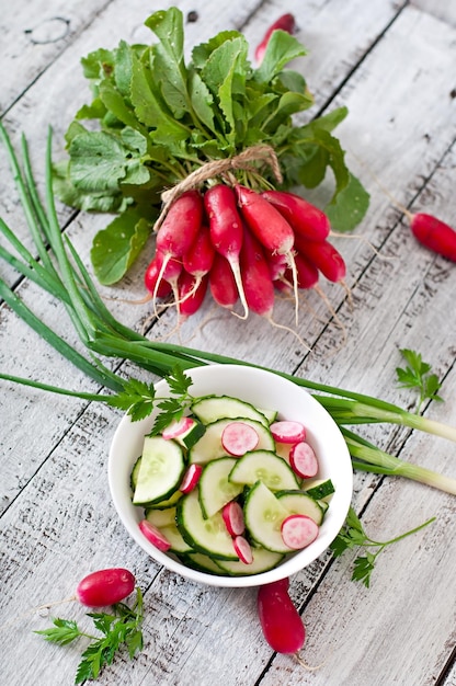 Verse salade van komkommers en radishes in een witte schaal op de oude houten achtergrond