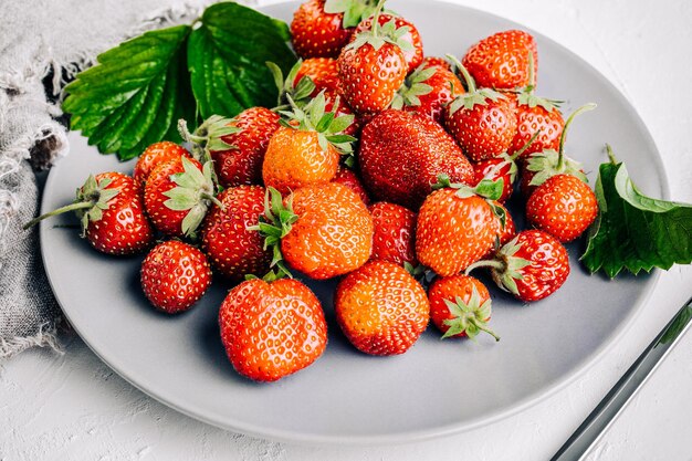 Verse, sappige aardbeien met bladeren op een witte betonnen ondergrond.