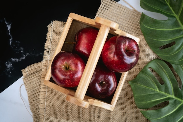 Foto verse, sappige rode appels in houten mand met monstera groen blad op een zak en zwart en wit marmer oppervlak voor aanstaande thanksgiving festival