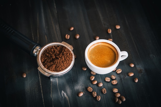 Verse smakelijke espresso kopje warme koffie met koffiebonen en koffiezetapparaat op donkere achtergrond