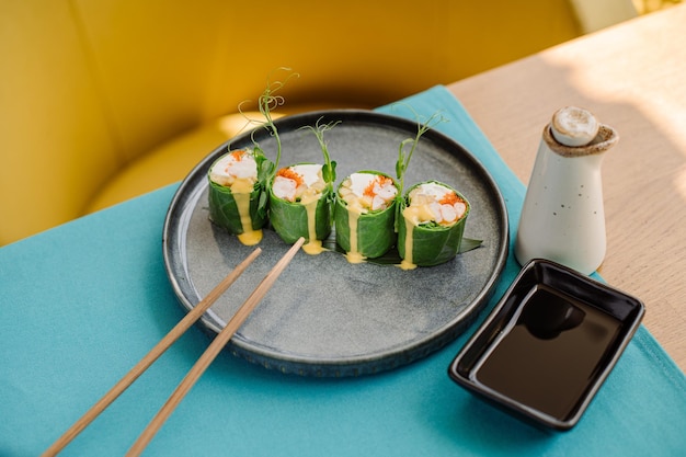 Verse smakelijke sushi-broodjes met groene bladeren, zalm en sappige saus op de tafel in het sushi-restaurant met prachtige contrastbliksem