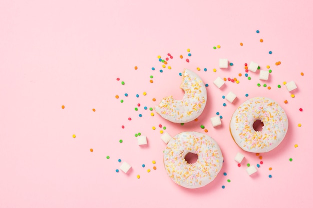 Verse smakelijke zoete donuts, veelkleurige decoratieve snoepjes, suikerklontjes op een roze achtergrond. Bakkerijconcept, vers gebak, heerlijk ontbijt, fastfood. Plat lag, bovenaanzicht.