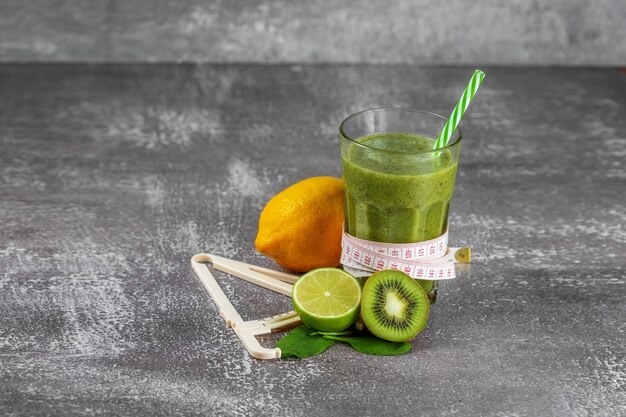 Verse smoothiedrank in een groot glasglas met een centimeter eromheen en een schuifmaat ernaast, omgeven door fruit op een grijze betonnen achtergrond. Het concept van goede voeding, gewichtsverlies