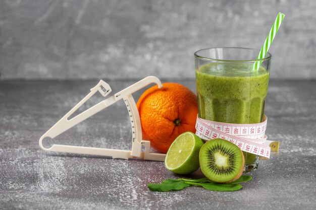 Verse smoothiedrank in een groot glasglas met een centimeter eromheen en een schuifmaat ernaast, omgeven door fruit op een grijze betonnen achtergrond. Het concept van goede voeding, gewichtsverlies