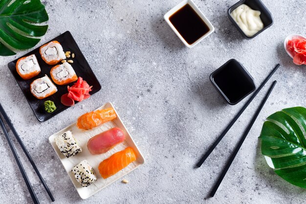 Verse sushi die op zwart-witte lei met metaalstokken, saus en groene bladeren worden geplaatst