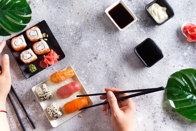 Verse sushi die op zwart-witte lei worden geplaatst, het metaalstokken van de handgreep, saus en groene bladeren