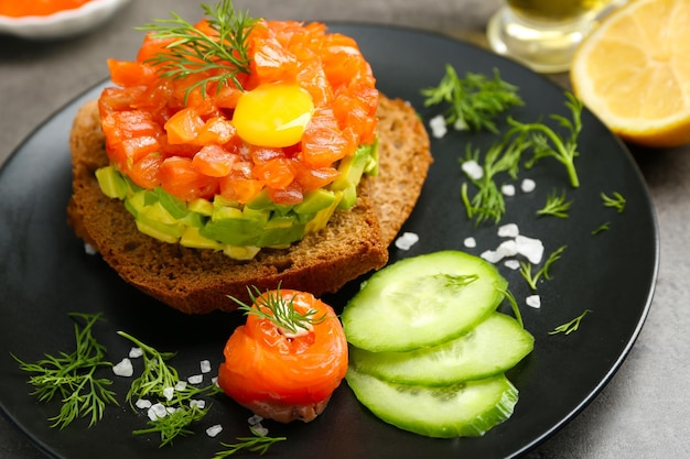 Verse tartaar met zalm avocado dooier en zwart brood op plaat close-up