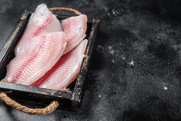 Verse tilapia witte visfilet in een houten dienblad Zwarte achtergrond Bovenaanzicht Ruimte kopiëren