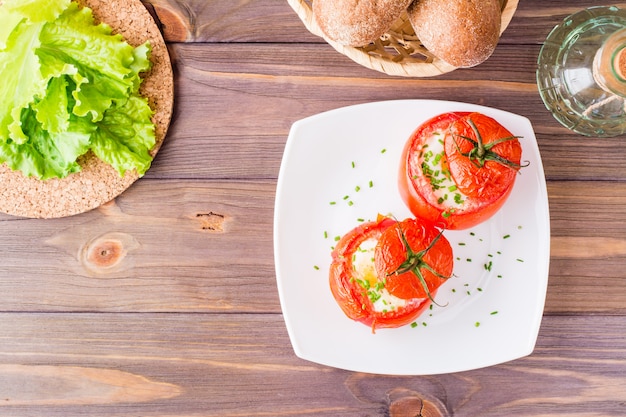 Verse tomaten gebakken met kaas en ei bestrooid met groene uien op een bord op een houten tafel. Bovenaanzicht Kopieer ruimte