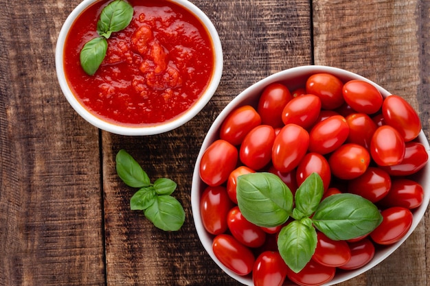 Verse tomaten in kom onold houten tafel. Tomatenachtergrond, gezonde groenten en basilicumbladeren.