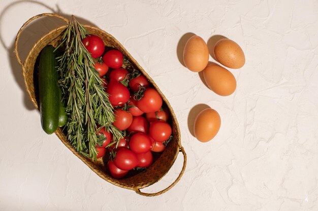 Verse tomaten komkommers kippeneieren en een paar takjes rozemarijn in een rieten mand