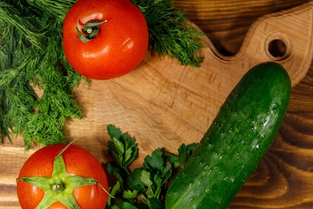 Verse tomaten, komkommers, peterselie en dille op snijplank op houten tafel