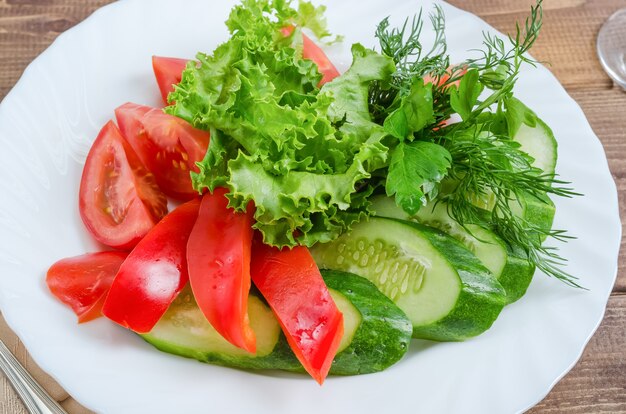 Verse tomaten met komkommers, sla en dille op een witte plaat close-up