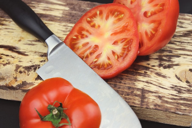 Verse tomaten op snijplank in een donkere achtergrond Koken gezonde maaltijd Close-up mes en tomaat op houten bord
