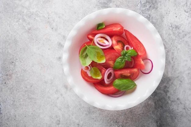 Verse tomatensalade met basilicumbladeren, olijfolie en ui in witte kom op lichte achtergrond Traditioneel italiaans of mediterraan voedseldieet Bovenaanzicht