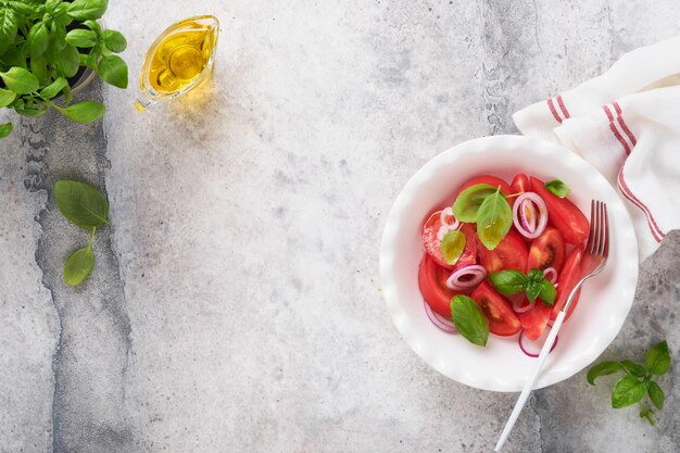 Verse tomatensalade met basilicumbladeren, olijfolie en ui in witte kom op lichte achtergrond Traditioneel italiaans of mediterraan voedseldieet Bovenaanzicht