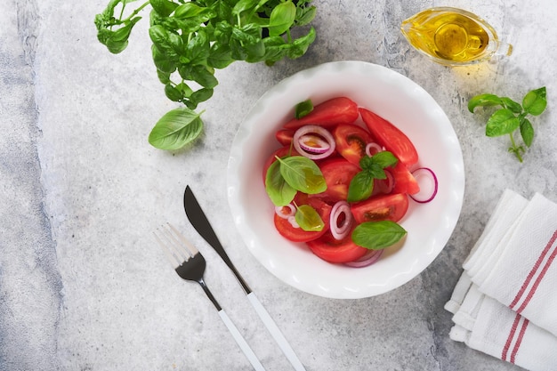 Verse tomatensalade met basilicumbladeren, olijfolie en ui in witte kom op lichte achtergrond Traditioneel italiaans of mediterraan voedseldieet Bovenaanzicht