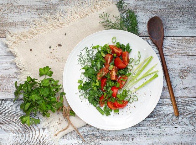 Verse veganistische salade van tomaat en groen met een bosje peterselie op een witte plaat een lichte houten tafel op een licht servet Uitzicht van bovenaf