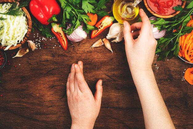 Verse veganistische vegetarische ingrediënten groenten specerijen kruiden voor gezond eten op rustieke houten keukentafel met snijplank Womens handen neemt oliefles Dieet schoon comfort eten koken concept