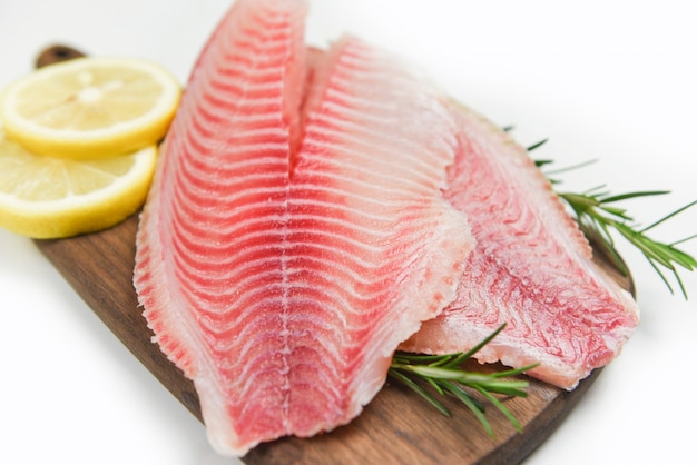 Verse visfilet gesneden voor biefstuk of salade met kruiden kruiden rozemarijn en citroen - Rauwe tilapia filet vis op houten snijplank en witte achtergrond en ingrediënten voor het koken van voedsel