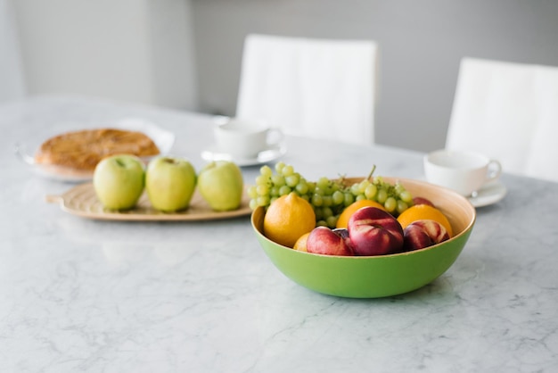 Verse vruchten perziken druiven en sinaasappels appel in een bord op de marmeren tafel in de keuken Gezond en gezond eten