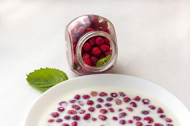 Verse wilde aardbeien met melk in een witte kom en glazen pot met bessen.