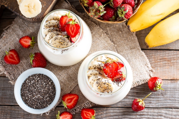 Verse yoghurt met aardbeien, banaan, chiazaden op een houten tafel, heerlijk dessert voor een gezond ontbijt. Bovenaanzicht