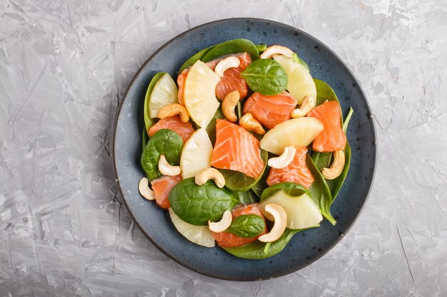 Verse zalm met ananas, spinazie en cashewnoten in blauwe keramische plaat op een grijs beton.