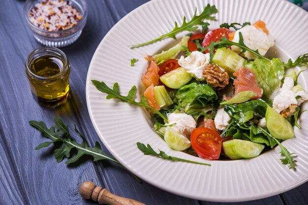 Verse zalmsalade met rode tomaten, zachte kaas, komkommer, noten en rucola